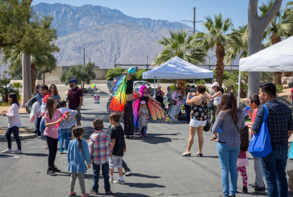 Families watching woman dressed like monarch butterfly on stilts.