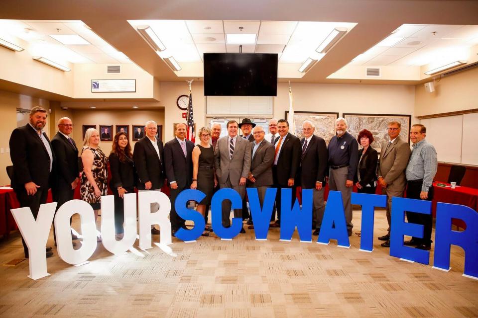 Group of people dressed formally in a board room in front of cut out letters that reads "Your SCV Water"